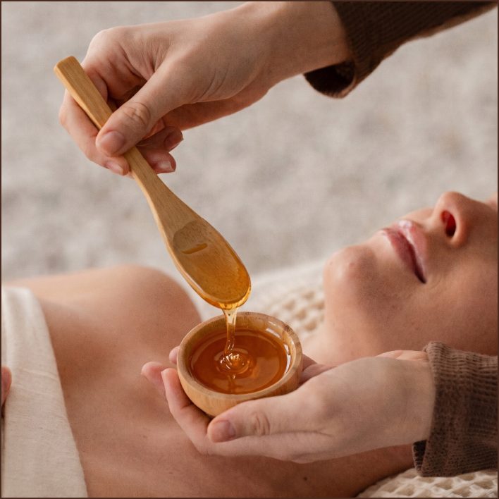 Esthetician pouring amber treatment gel from a bamboo spoon beside a draped client